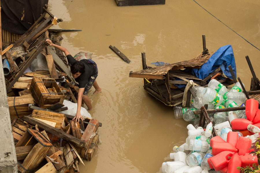 Photo of a man trying to gather scattered possessions in the wake of a flood.