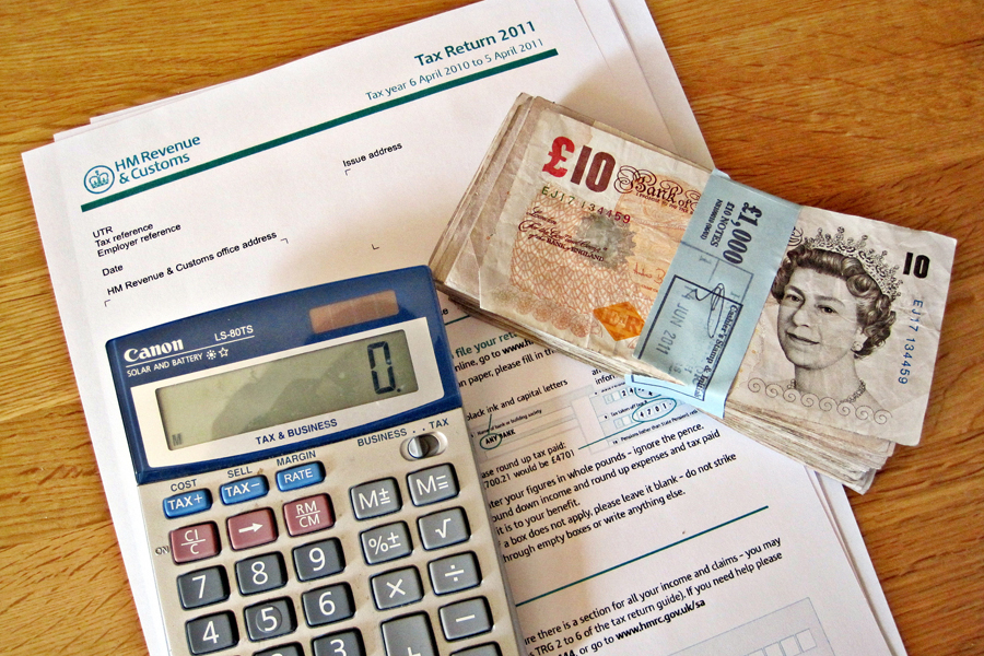 Photo of a tabletop filled with tax forms, money, and a calculator.