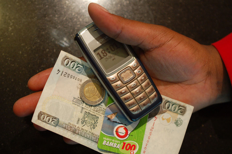 Photo of a hand holding a mobile phone, cash, and a calling card.